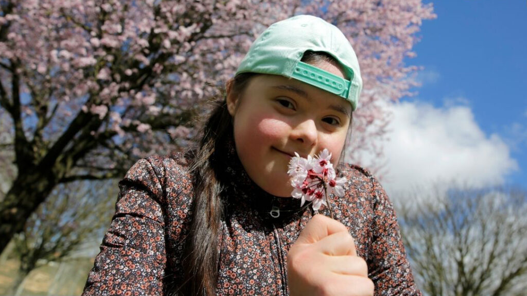 Une enfant sourit en respirant une fleur